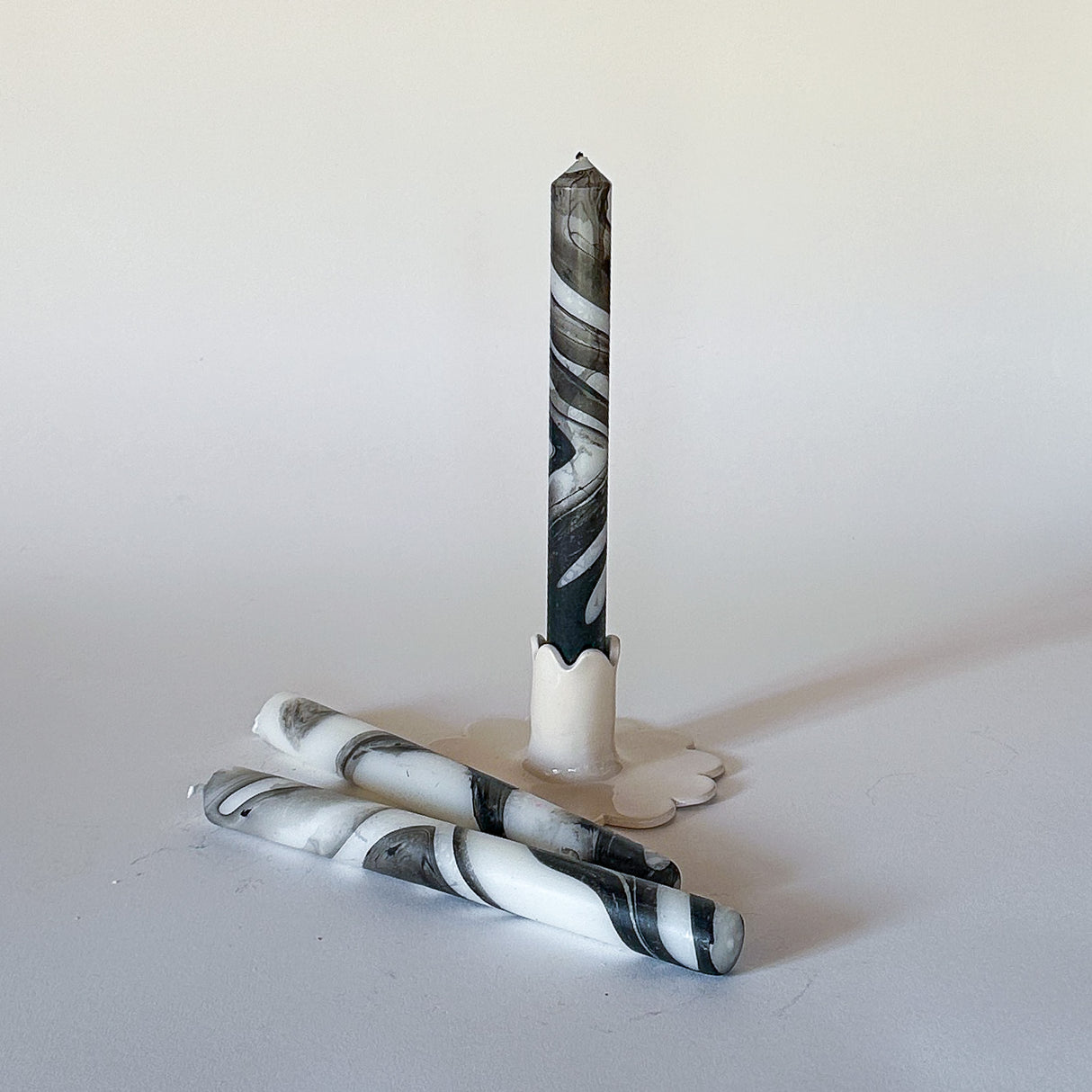 Three marbled black-and-white taper candles on a light background, set in a way that one candle is upright and the others are lying horizontally.