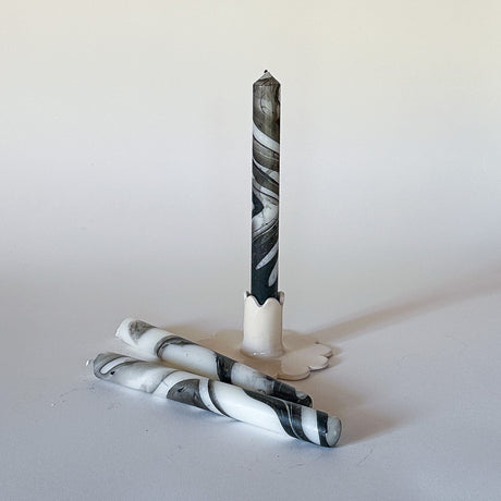 Three marbled black-and-white taper candles on a light background, set in a way that one candle is upright and the others are lying horizontally.