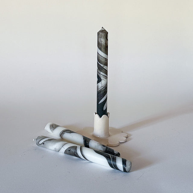 Three marbled black-and-white taper candles on a light background, set in a way that one candle is upright and the others are lying horizontally.