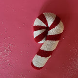 Candy cane–shaped decorative pillow with red and white stripes, made from a textured hooked fabric and displayed against a red background.