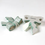 Two ceramic bow decorations with green and white stripes on a white background