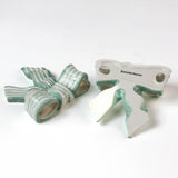 Two ceramic bow decorations with green and white stripes on a white background