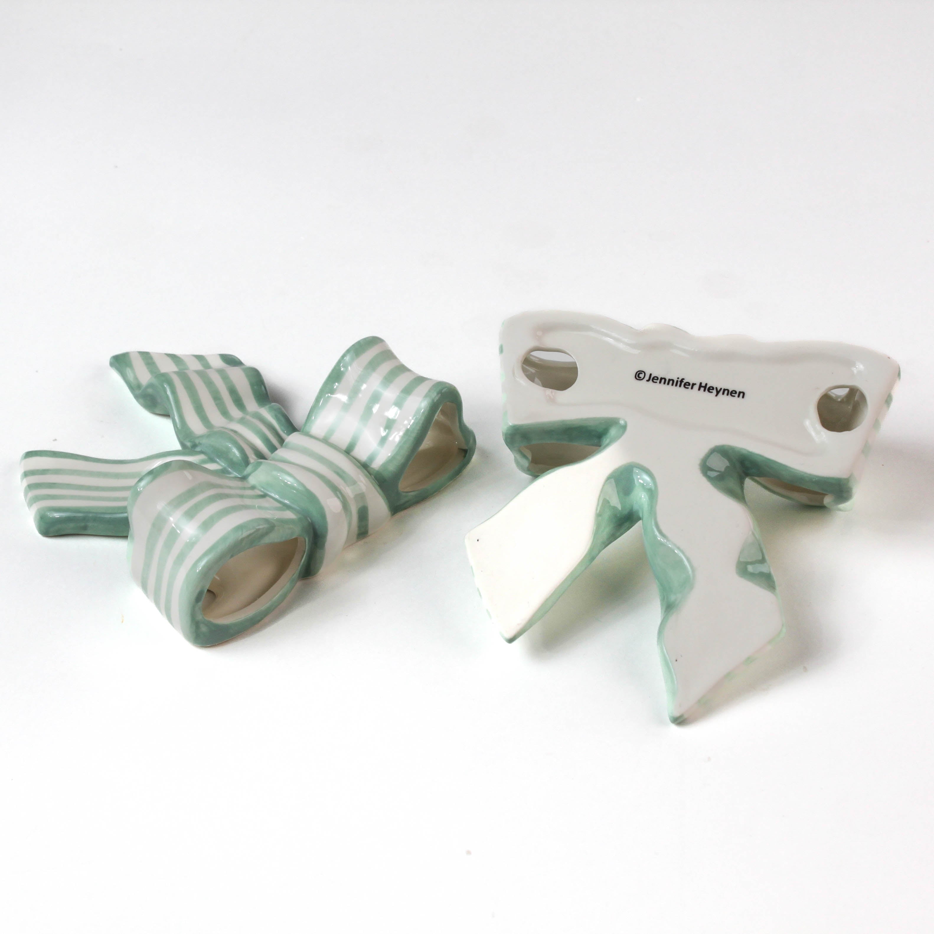 Two ceramic bow decorations with green and white stripes on a white background