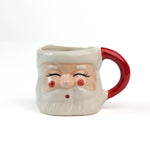 Ceramic Christmas santa mug with a jolly santa face design with red cheeks and a red handle on a white background