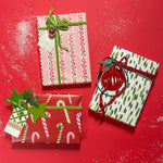 Three christmas gifts wrapped in colorful christmas wrapping paper from Madcap Cottage on a red background.