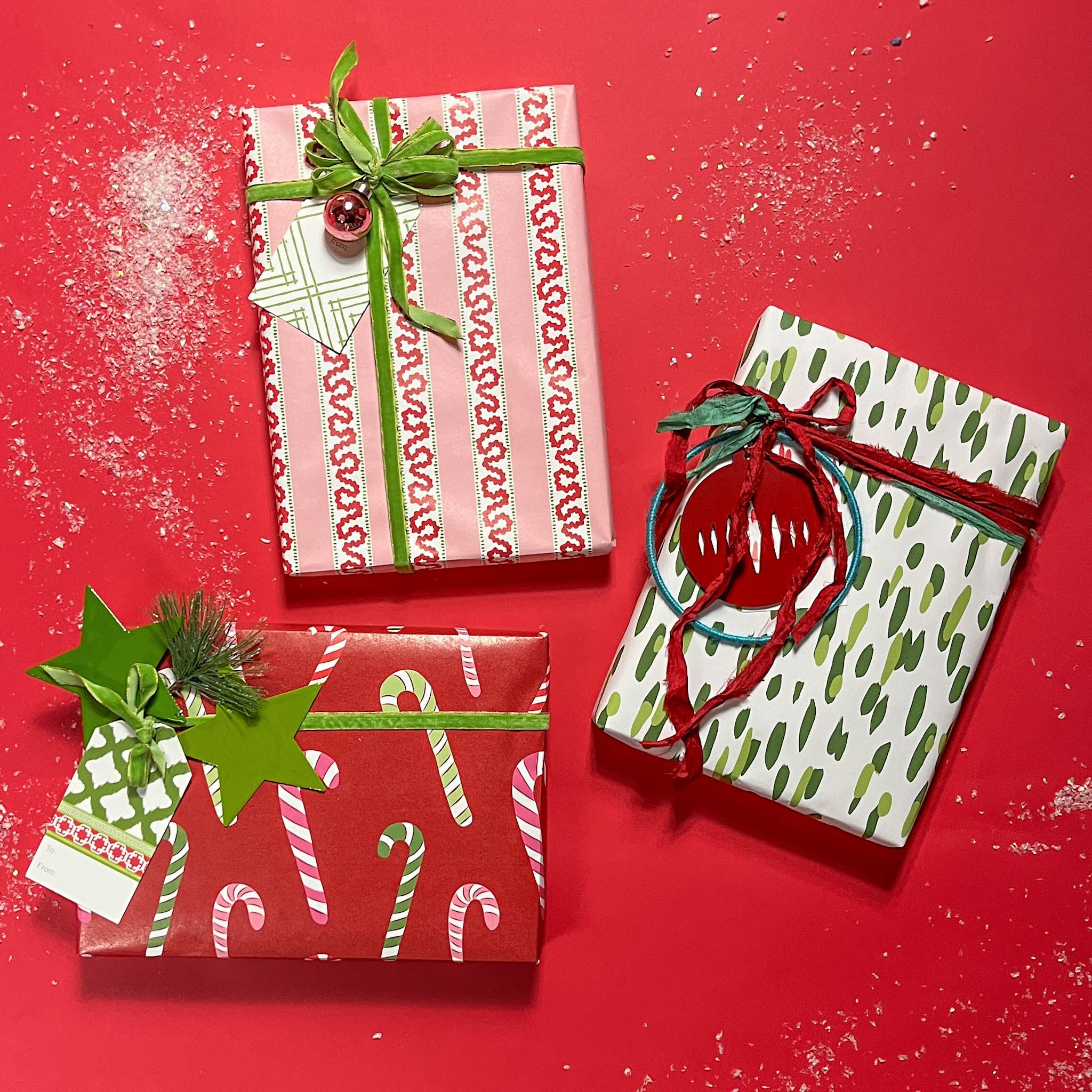 Three christmas gifts wrapped in colorful christmas wrapping paper from Madcap Cottage on a red background.