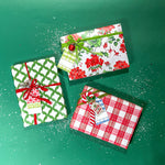 Three christmas gifts wrapped in colorful christmas wrapping paper from Madcap Cottage on a green background.