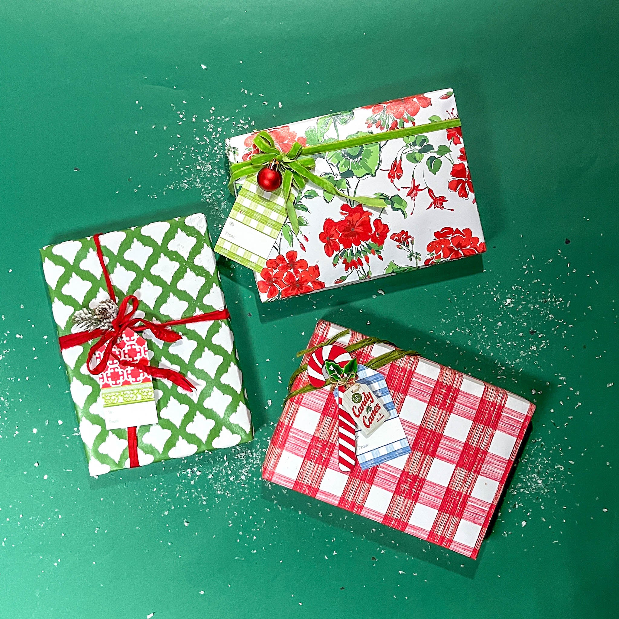 Three christmas gifts wrapped in colorful christmas wrapping paper from Madcap Cottage on a green background.