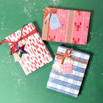 Three christmas gifts wrapped in colorful christmas wrapping paper from Madcap Cottage on a green background.