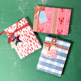 Three christmas gifts wrapped in colorful christmas wrapping paper from Madcap Cottage on a green background.