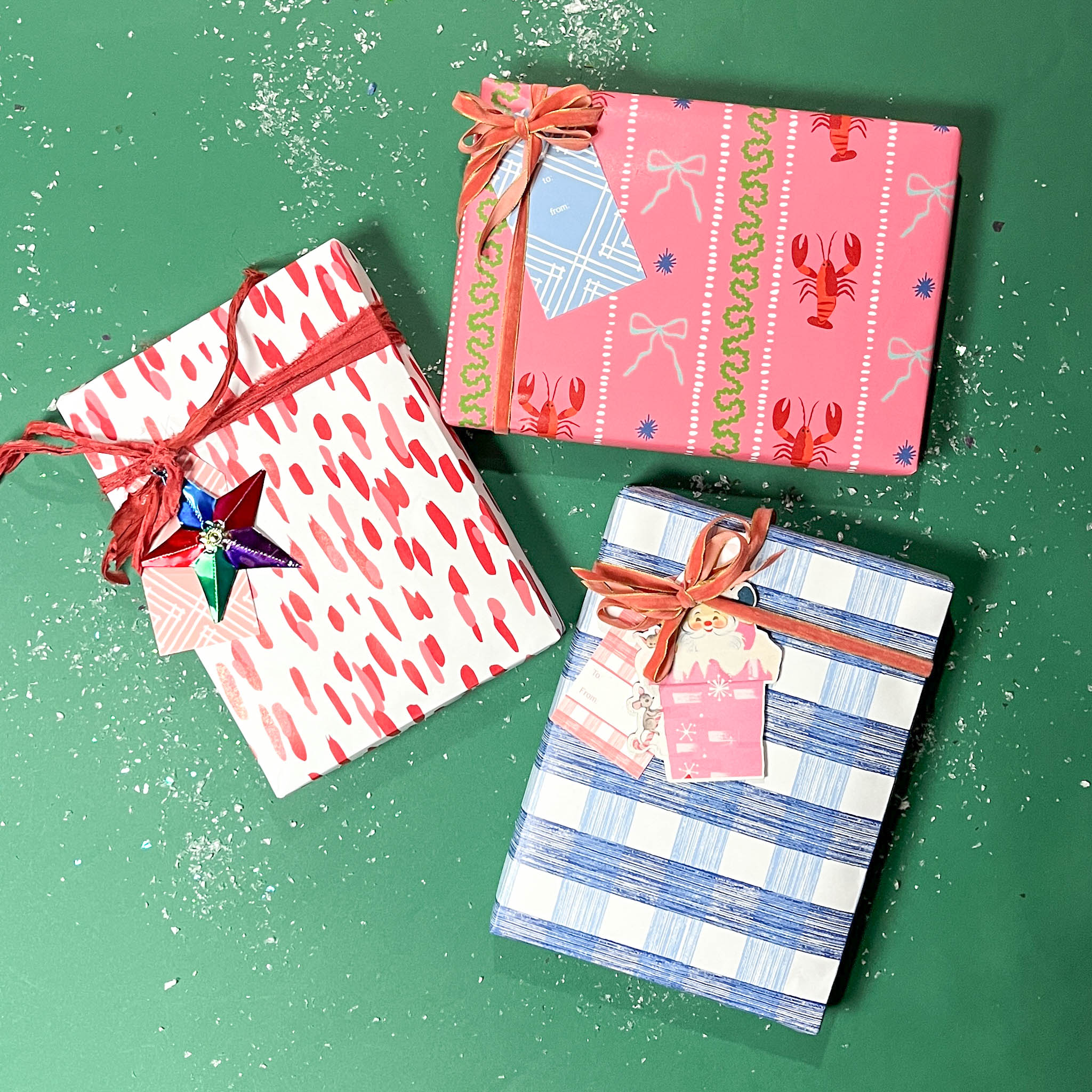 Three christmas gifts wrapped in colorful christmas wrapping paper from Madcap Cottage on a green background.
