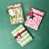 Three christmas gifts wrapped in colorful christmas wrapping paper from Madcap Cottage on a green background.