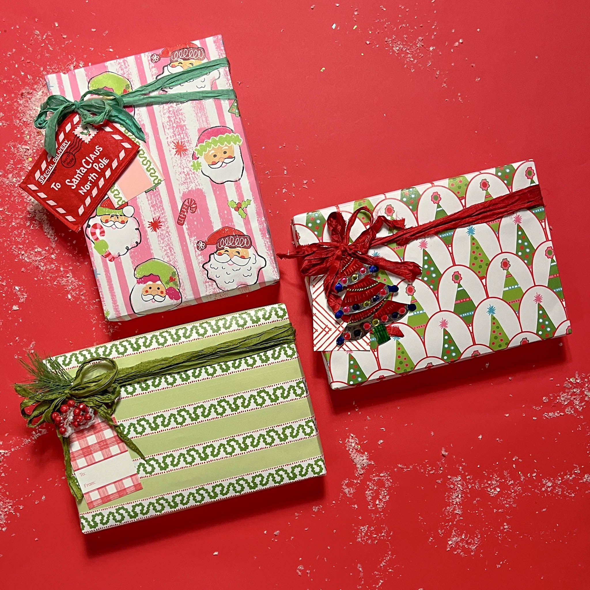 Three christmas gifts wrapped in colorful christmas wrapping paper from Madcap Cottage on a red background.
