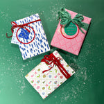 Three christmas gifts wrapped in colorful christmas wrapping paper from Madcap Cottage on a green background.