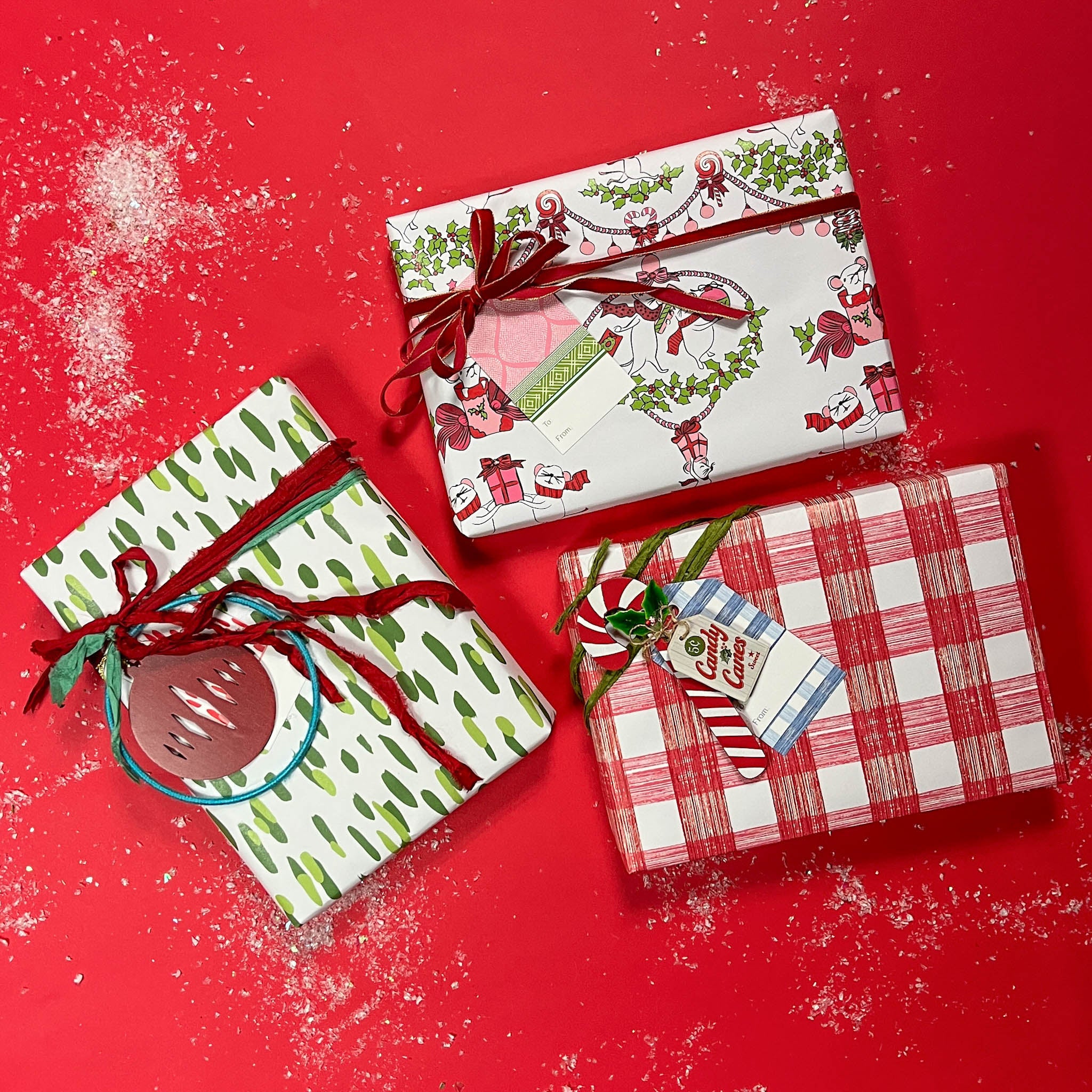 Three christmas gifts wrapped in colorful christmas wrapping paper from Madcap Cottage on a red background.
