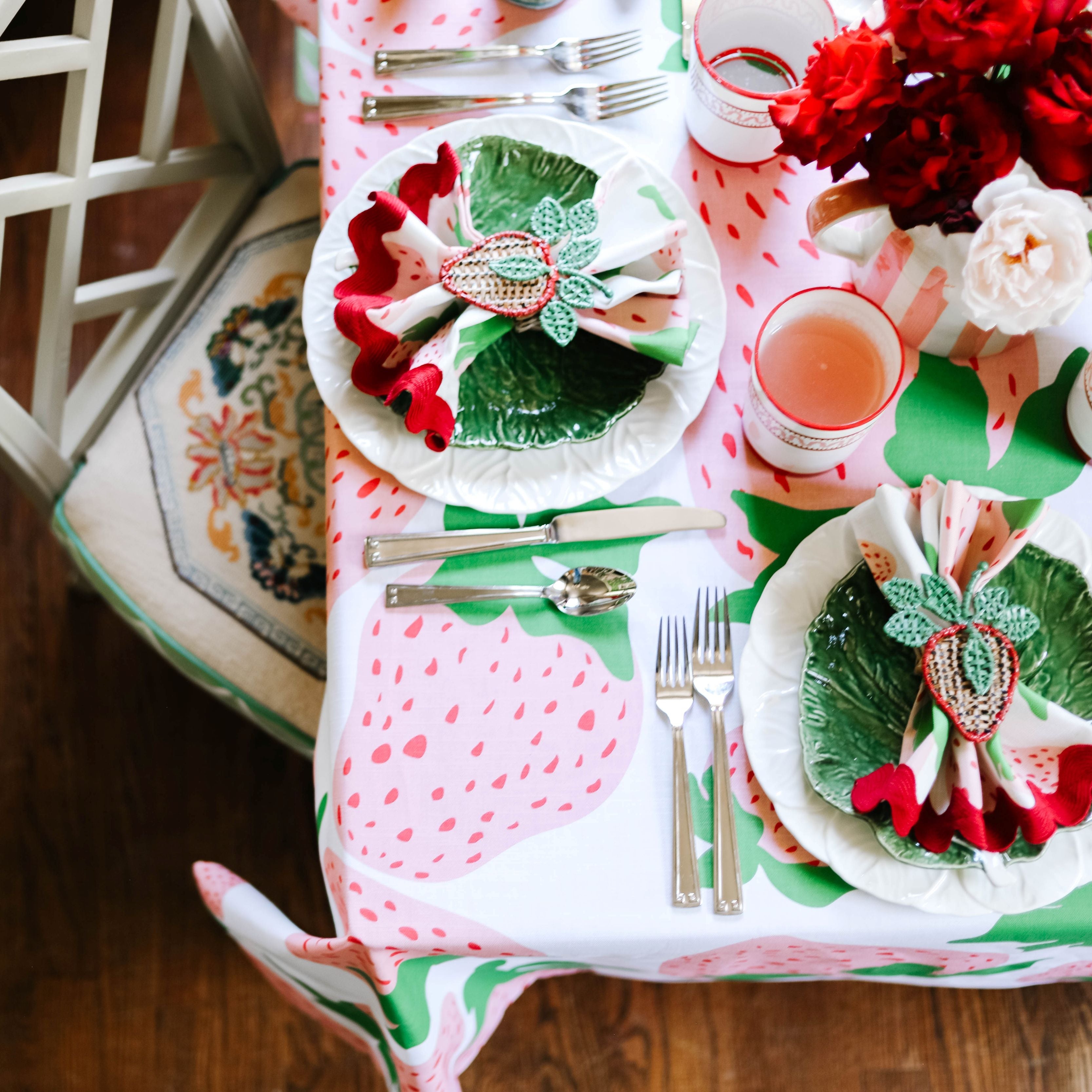 Bright dining table setting with strawberry-print tablecloth, green leaf plates, folded napkins, and pink drinks for entertaining.