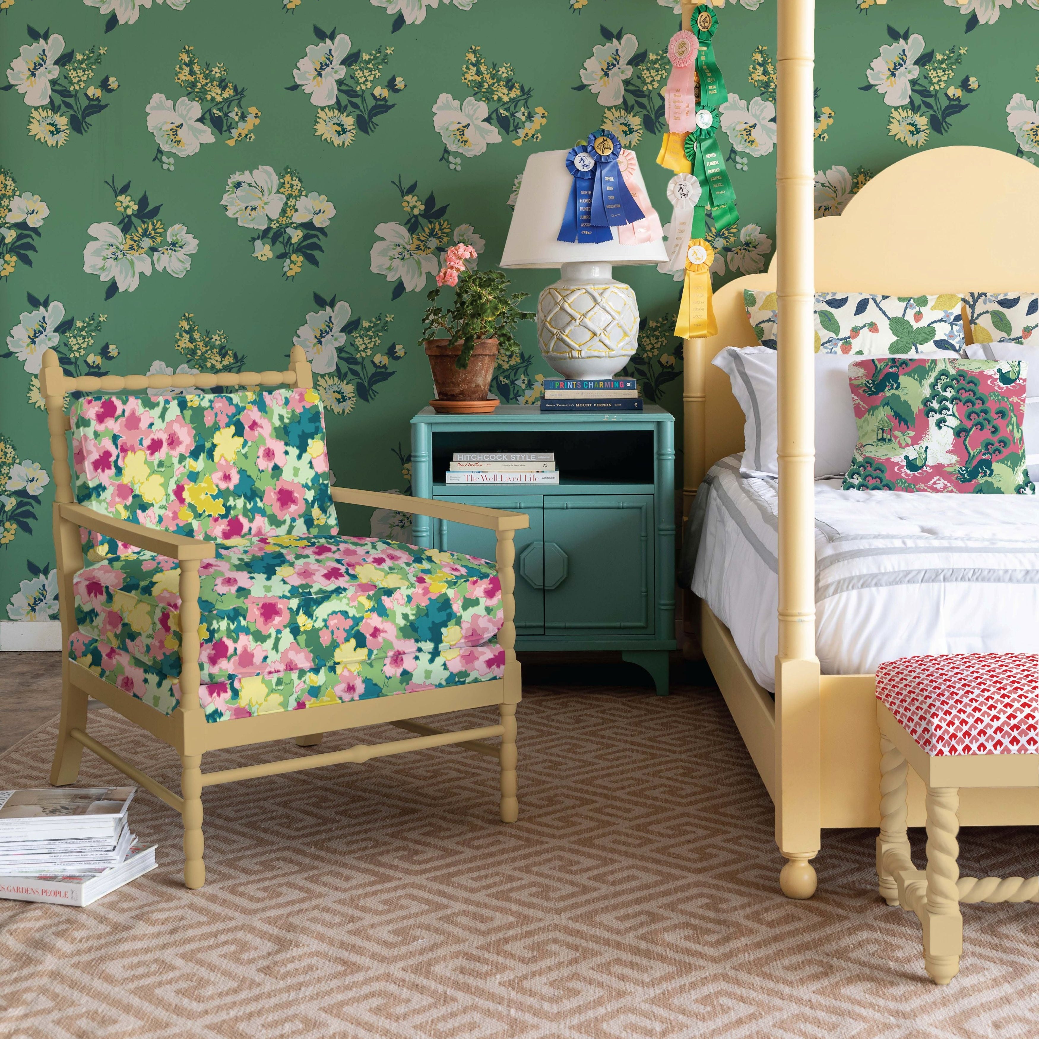 Green floral wallpaper styled bedroom with yellow four-poster bed, patterned armchair, and layered botanical textiles.
