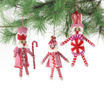 Three Christmas felt nutcracker ornaments in red and white striped outfits hanging from a christmas tree branch