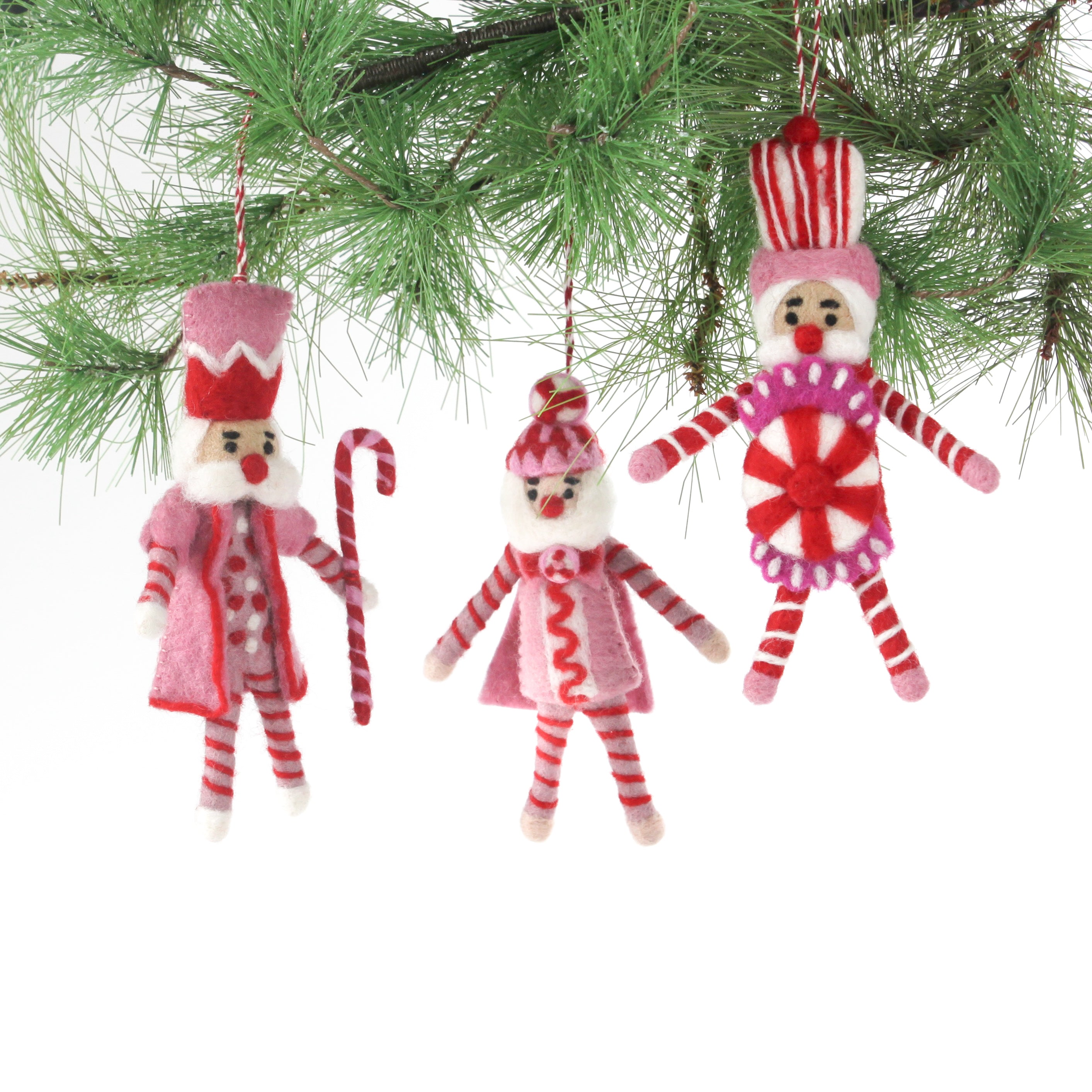 Three Christmas felt nutcracker ornaments in red and white striped outfits hanging from a christmas tree branch