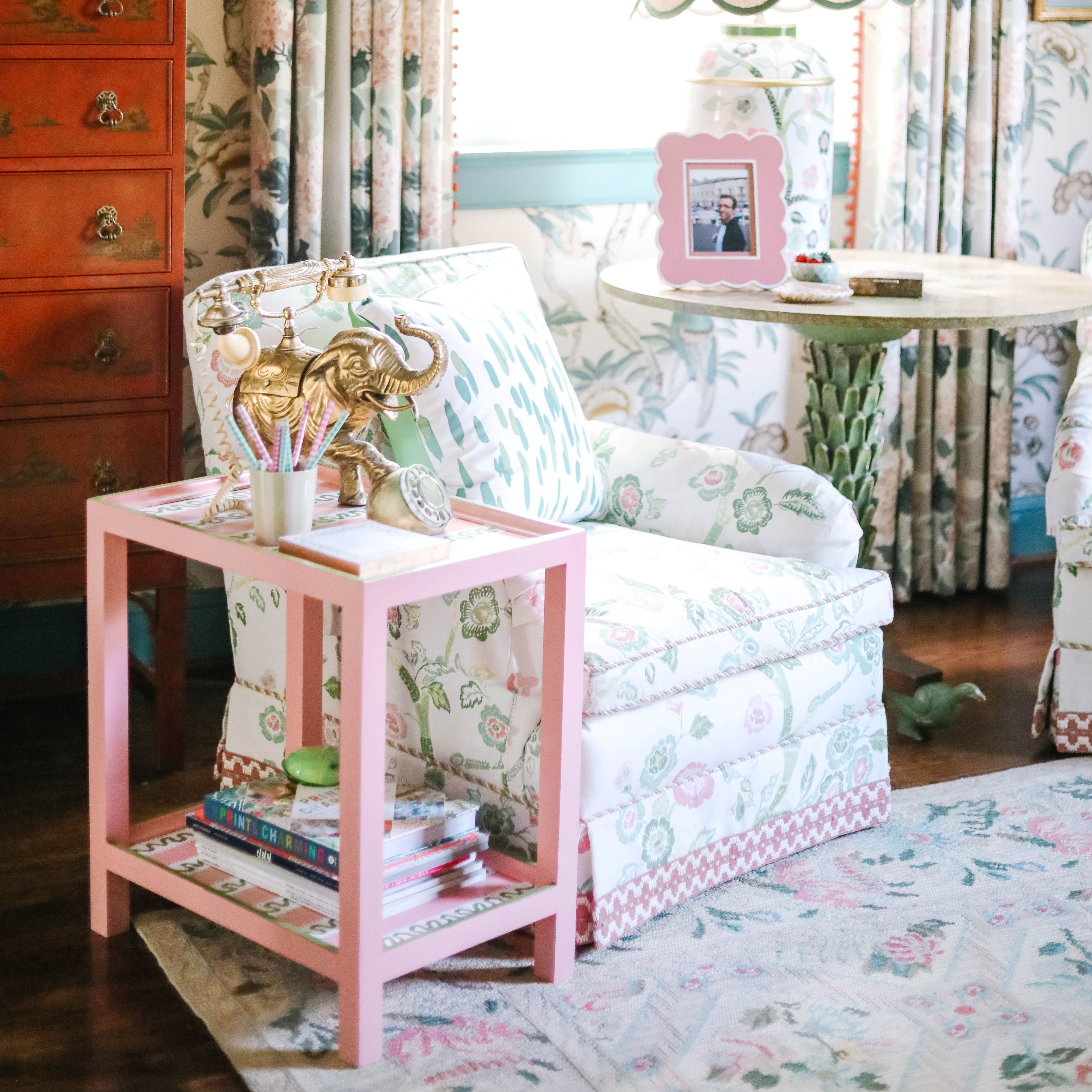 Colorful living room vignette with floral upholstery, patterned curtains, vintage dresser, and layered pastel decor.