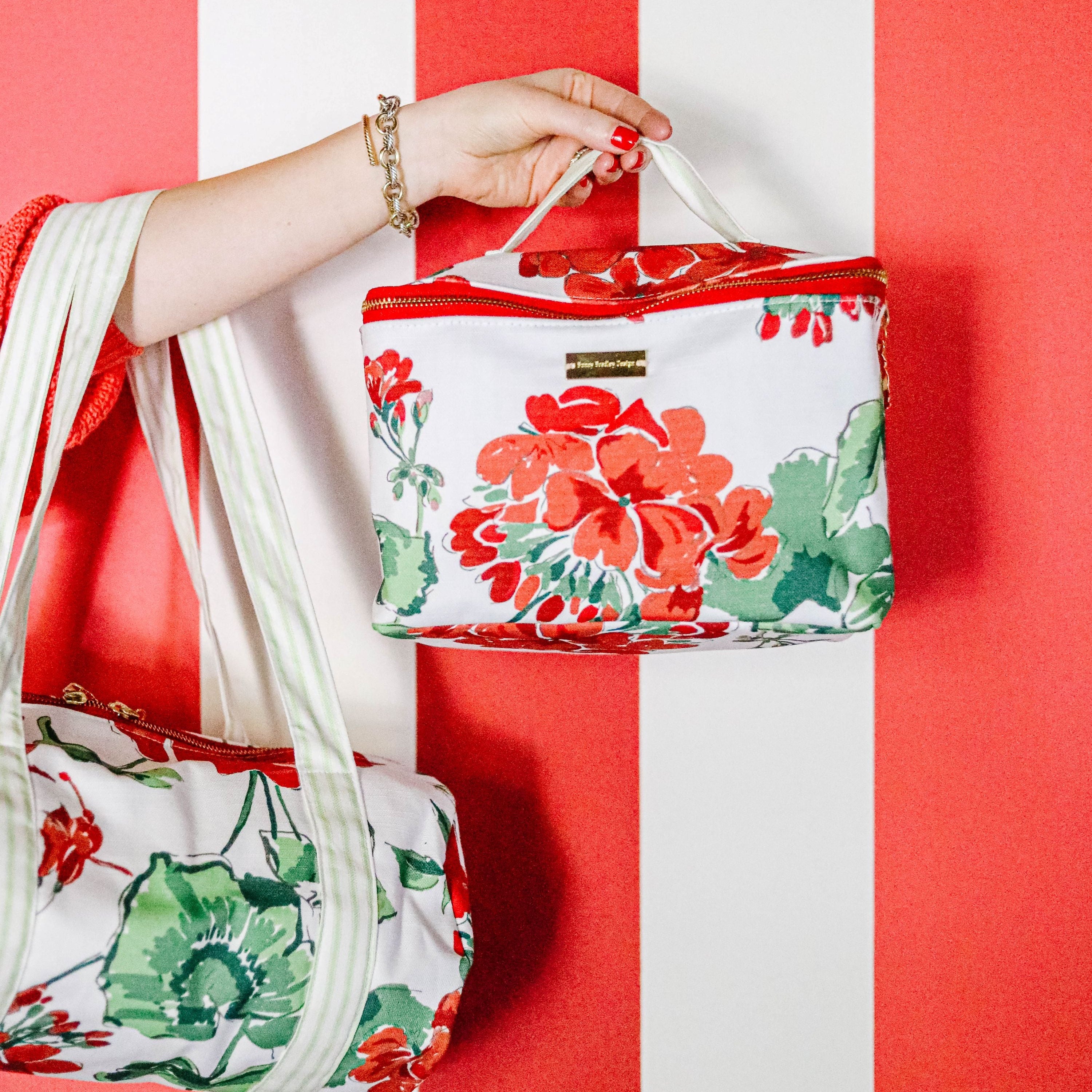 Floral cosmetic pouch and matching tote bag with red geranium  print against a red and white striped background.