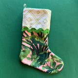A pink and green Christmas stocking with a palm leaf print and geometric printed folded top