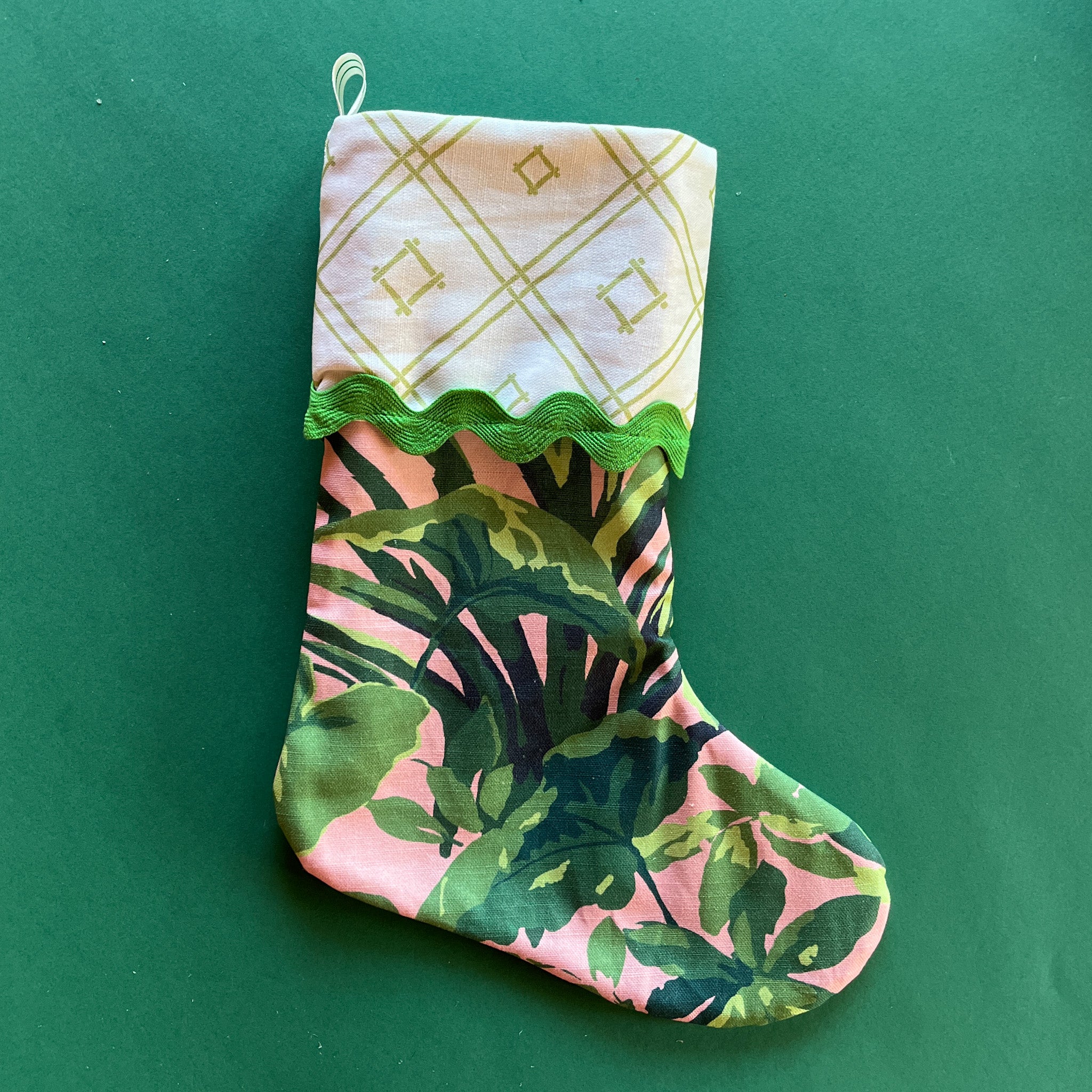 A pink and green Christmas stocking with a palm leaf print and geometric printed folded top