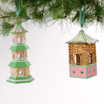 two miniature rattan pagoda chinoiserie christmas ornaments with green and pink painted accents from the brand madcap cottage hanging on a christmas tree branch. 