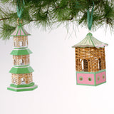 two miniature rattan pagoda chinoiserie christmas ornaments with green and pink painted accents from the brand madcap cottage hanging on a christmas tree branch. 