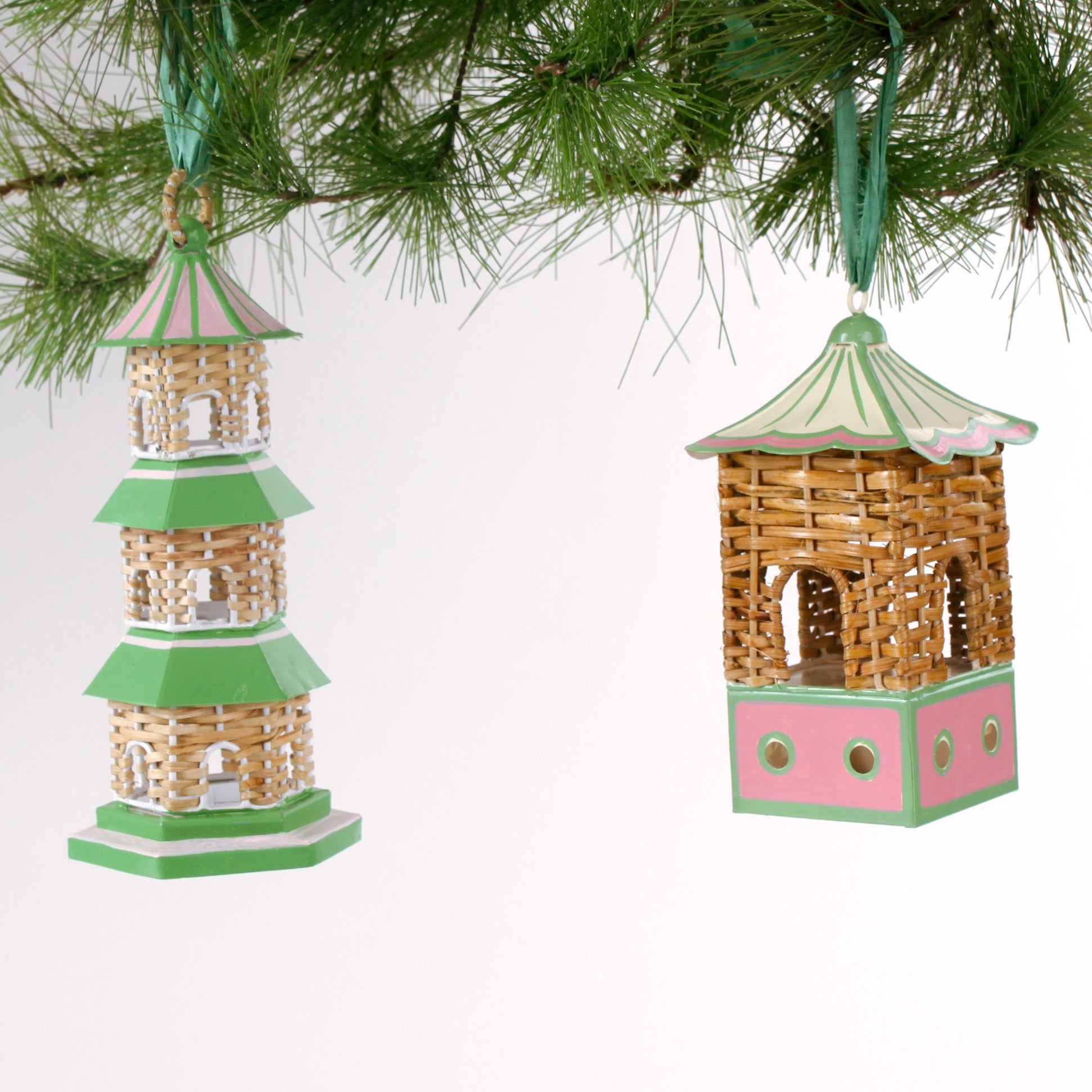two miniature rattan pagoda chinoiserie christmas ornaments with green and pink painted accents from the brand madcap cottage hanging on a christmas tree branch. 