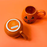 Orange ceramic mugs with a jack o'lantern design, one with a handle, one showing the bottom and the other is the top.