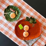 a large orange pumpkin serving platter with 5 halloween cookies on it against an orange paper halloween table runner. 