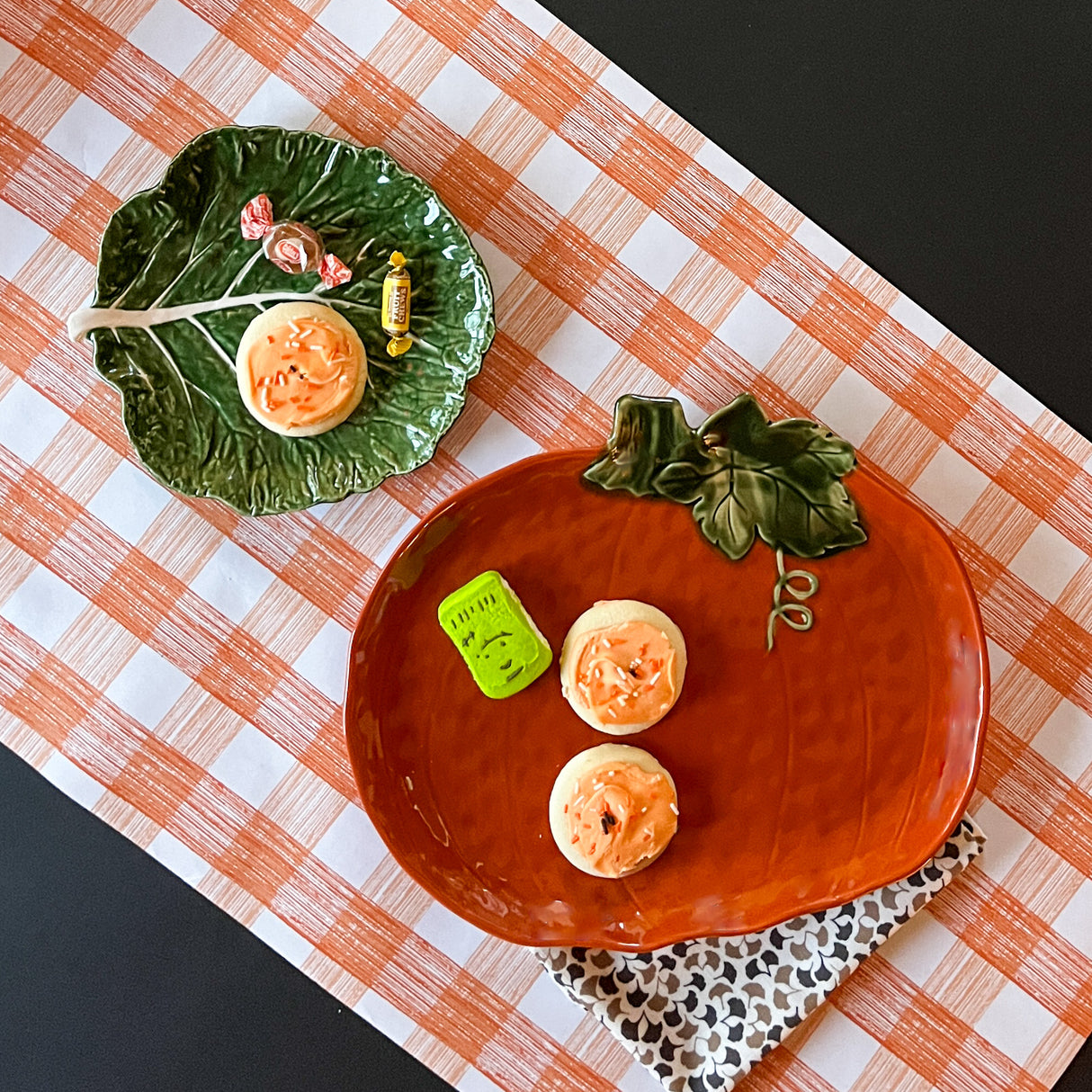 a large orange pumpkin serving platter with 5 halloween cookies on it against an orange paper halloween table runner. 