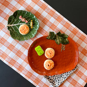 a large orange pumpkin serving platter with 5 halloween cookies on it against an orange paper halloween table runner. 