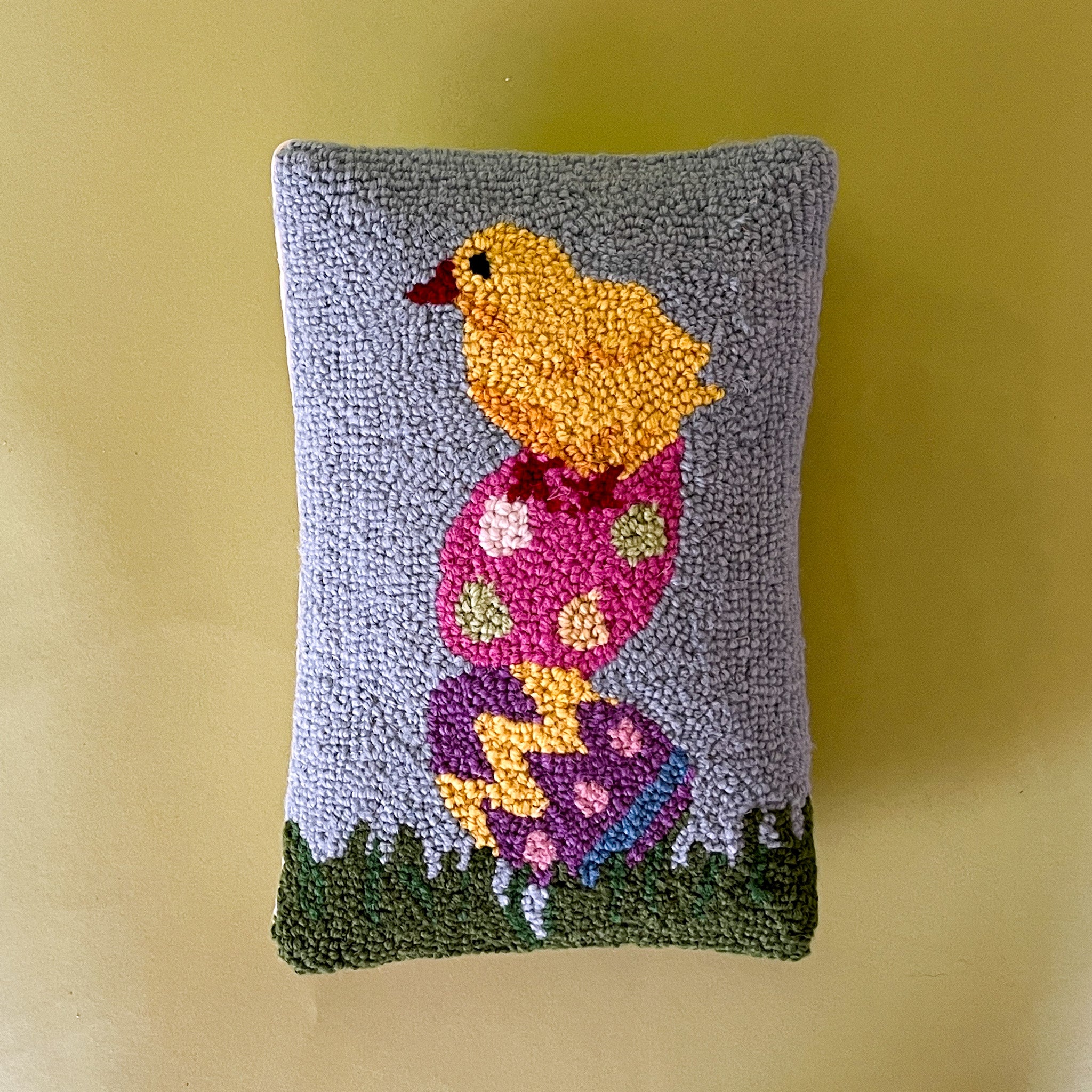 A purple easter pillow with two easter eggs with a yellow chick on top