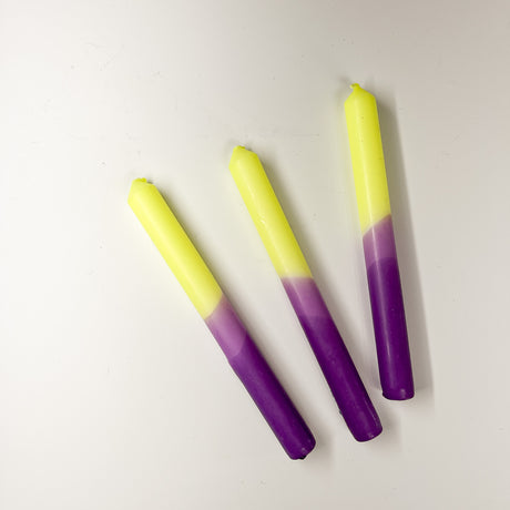 Three taper candles with a purple and yellow gradient, are lying horizontally.