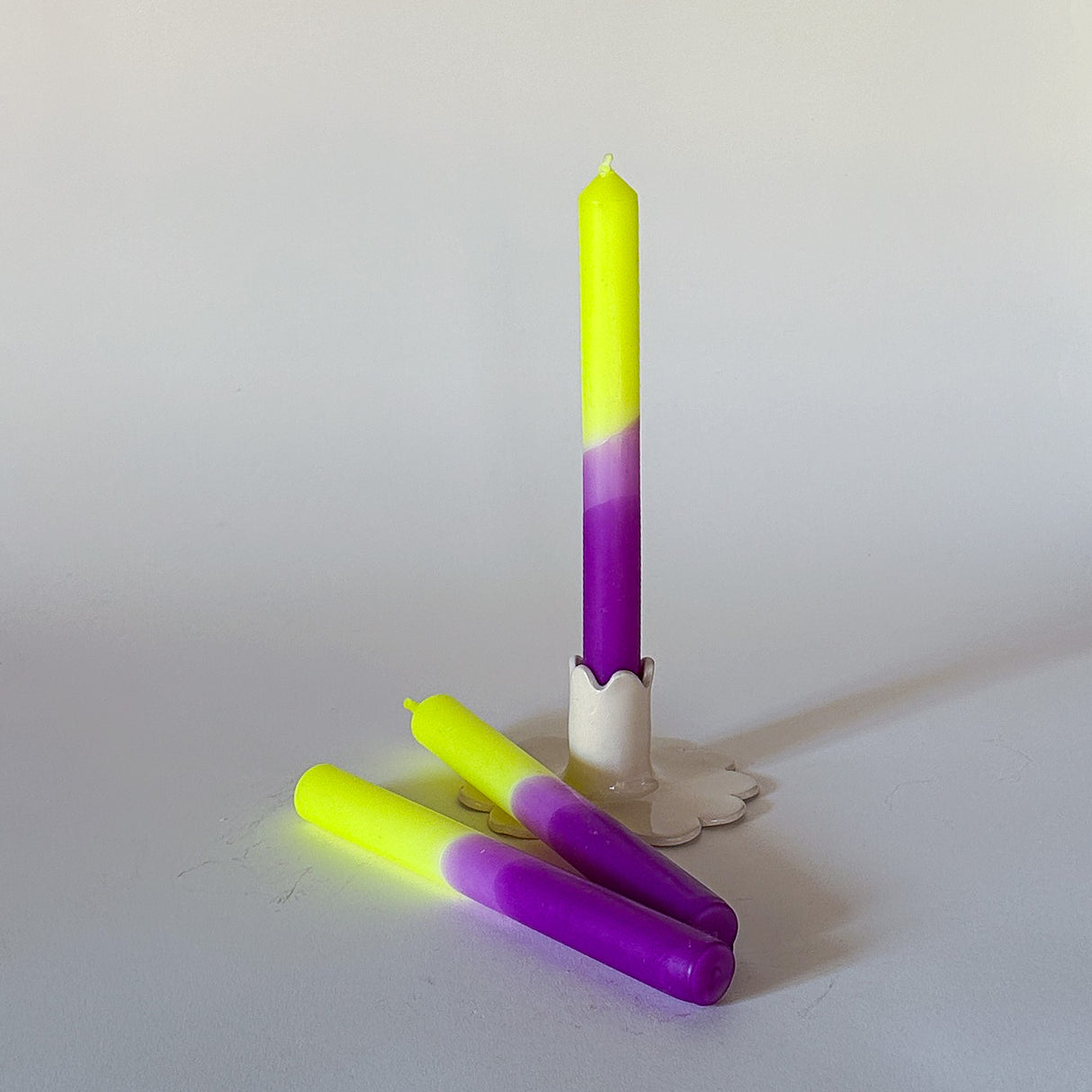 Three taper candles with a purple top and green bottom, displayed on a white surface.