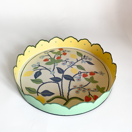 A round tole tray designed by Madcap Cottage with scalloped edges and a handpainted strawberry, blue flower and lemon motifs on the base