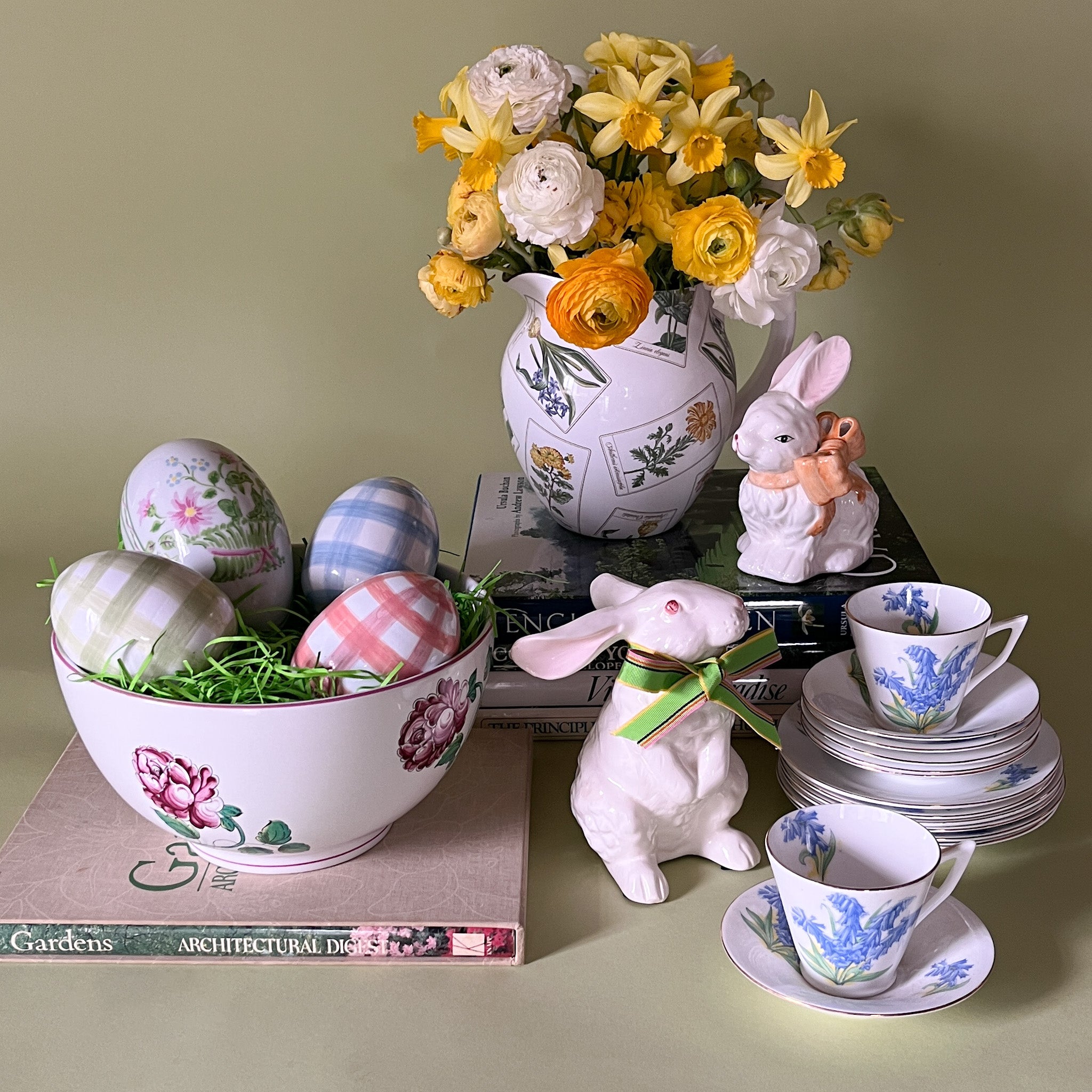 Vintage Easter tabletop decor featuring ceramic bunnies, painted eggs, floral china teacups, and a flower-filled pitcher.