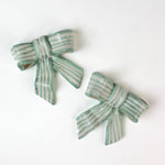 Two ceramic bow decorations with green and white stripes on a white background