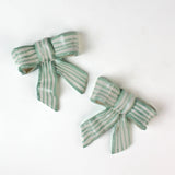 Two ceramic bow decorations with green and white stripes on a white background
