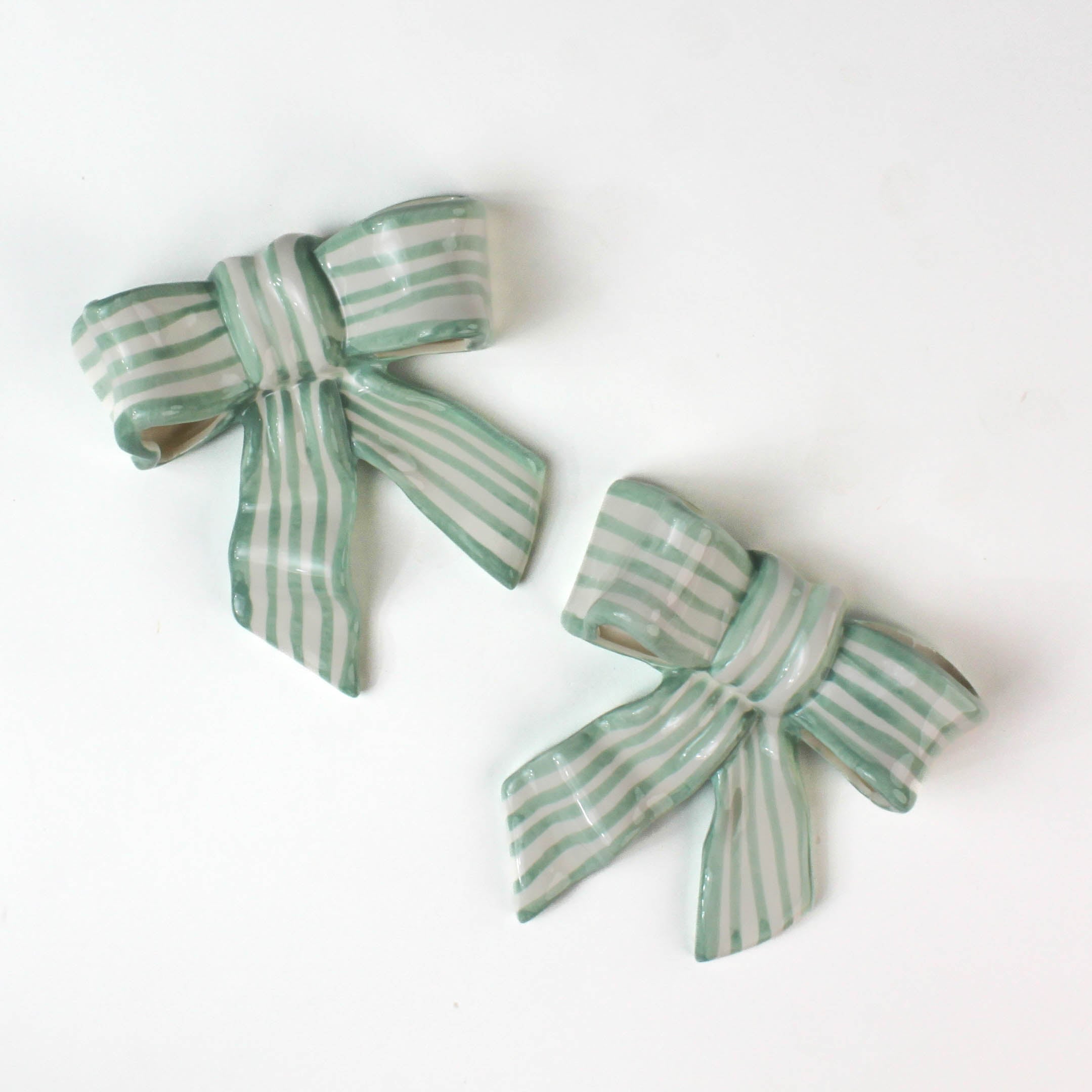 Two ceramic bow decorations with green and white stripes on a white background