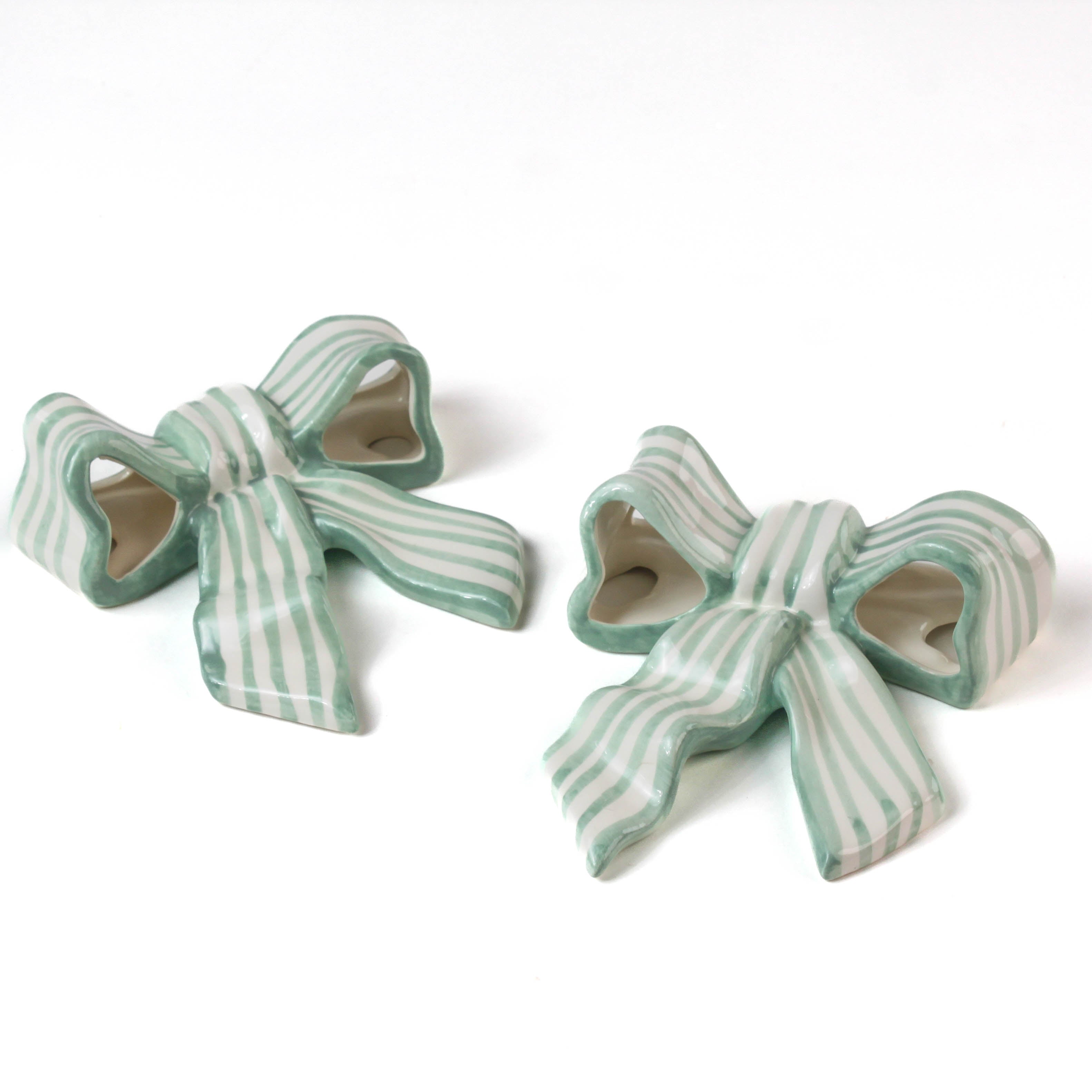 Two ceramic bow decorations with green and white stripes on a white background