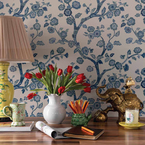 A desk featuring a tulip filled vase against blue and white chinoiserie wallpaper