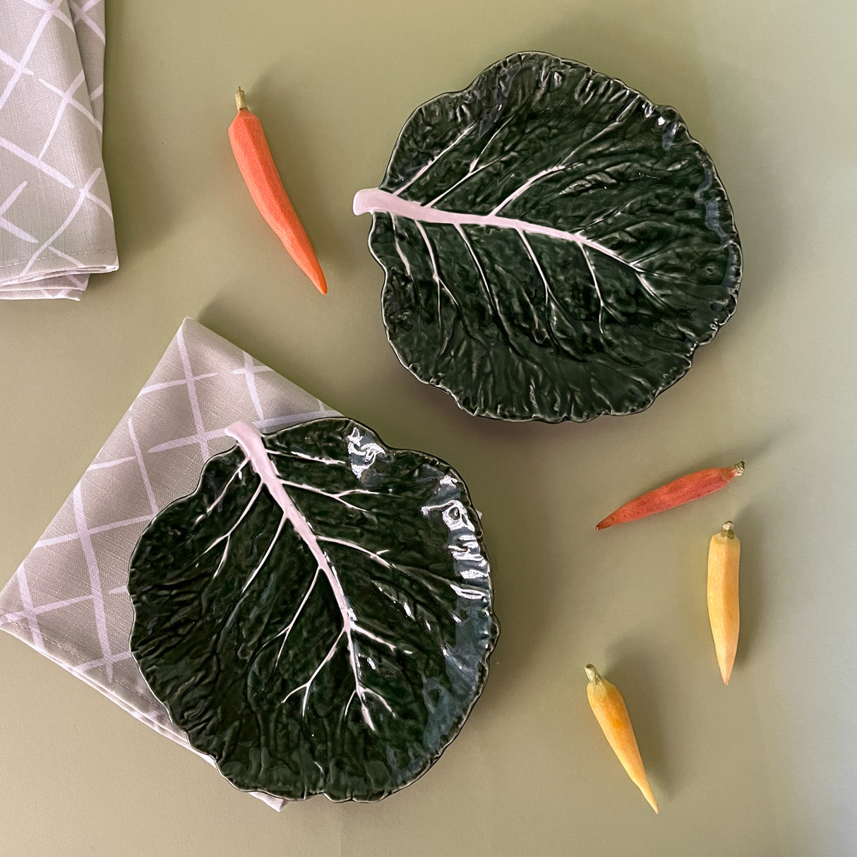 two ceramic cabbage leaf plates surrounded by carrots and napkins from madcap Cottage