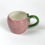 a pink ceramic strawberry mug with a green leafy handle