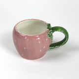 a pink ceramic strawberry mug with a green leafy handle