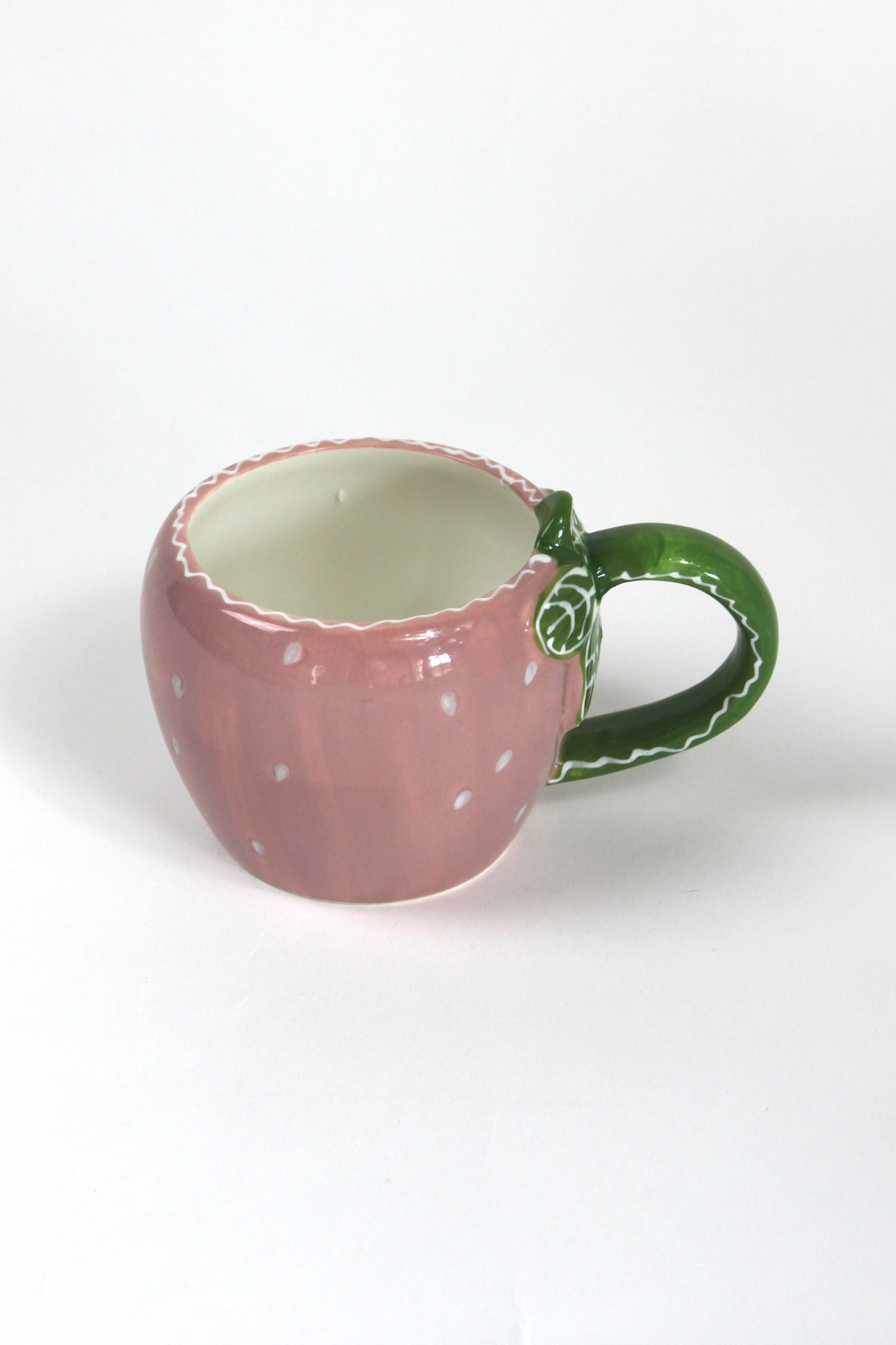 a pink ceramic strawberry mug with a green leafy handle