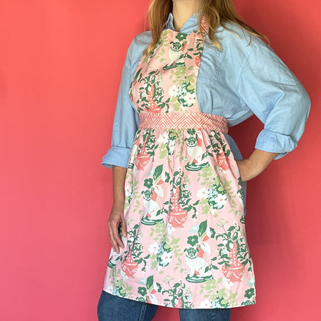 a woman wearing a pink and green chinoiserie apron featuring the Imperial Palace pattern from madcap cottage