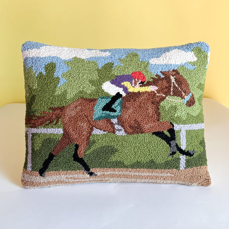a hooked wool derby day pillow featuring a brown race horse and hockey against a background of trees and blue sky